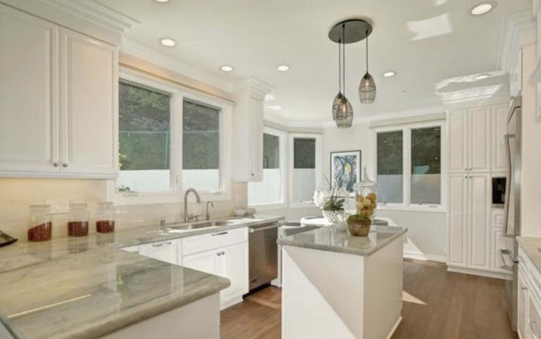 White kitchen with gray counters and three pendant lights.