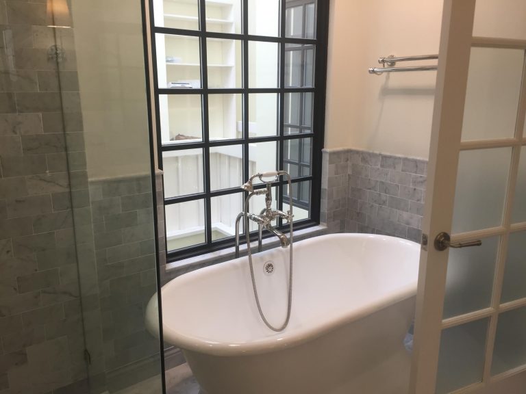 Freestanding bathtub beneath a black-framed window beside a towel ladder.