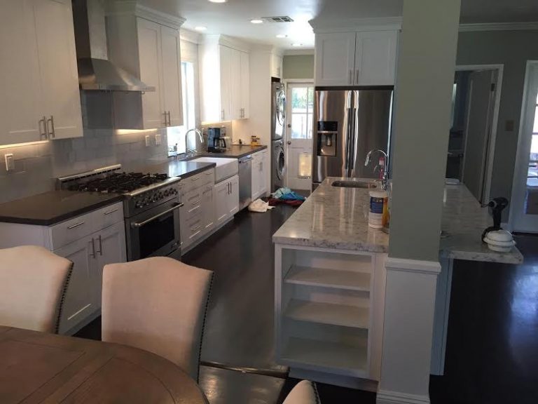 Completed white kitchen with island seating, dark counters and stainless steel appliances.
