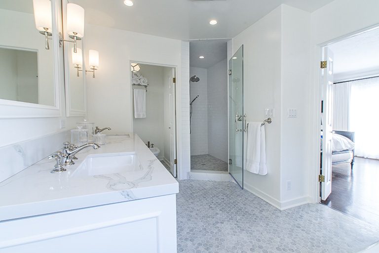 Double vanity with pale counters beside the glass shower.