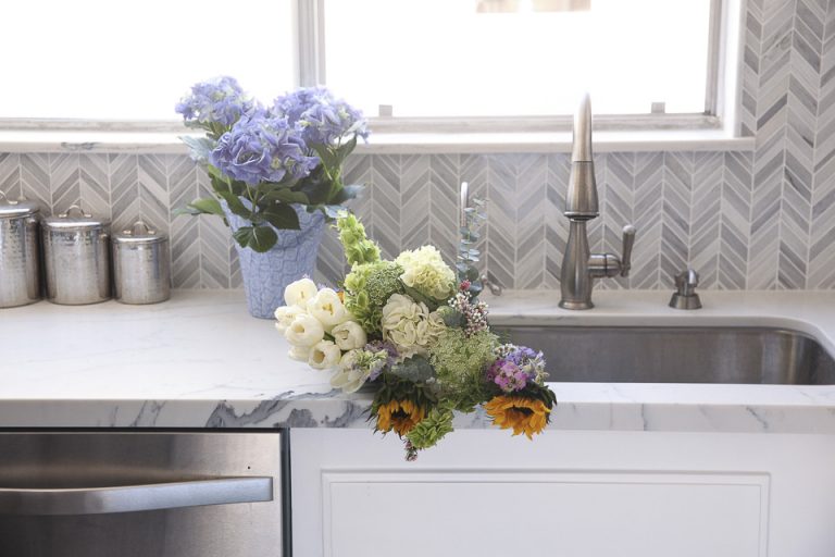 Kitchen sink with flowers beside a stainless dishwasher.