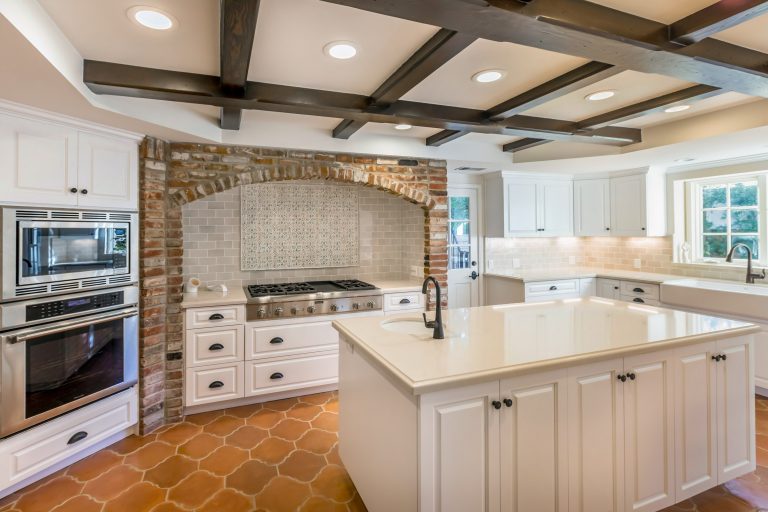 Kitchen island between wall ovens and white sink cabinets.
