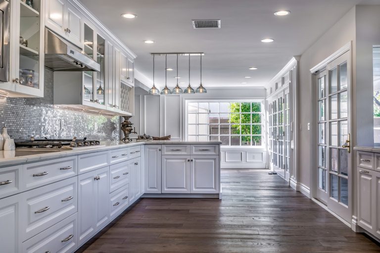 Long white kitchen with mosaic backsplash and wood flooring.