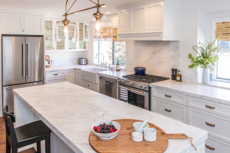 White kitchen with a marble island, pendant lights and glass-front cabinets.