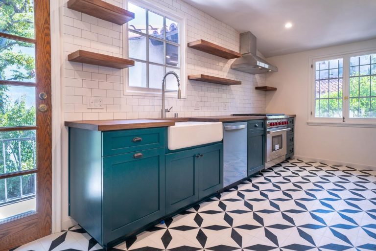 Blue kitchen cabinets with a farmhouse sink, wood shelves and patterned floor.
