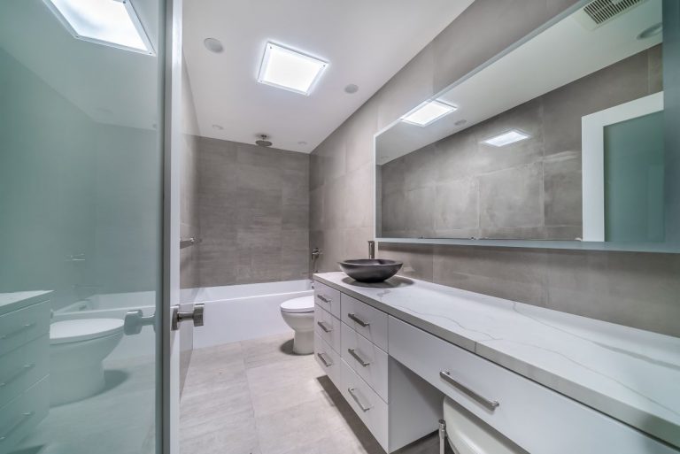 Gray-tiled bathroom with a long white vanity and overhead skylight.