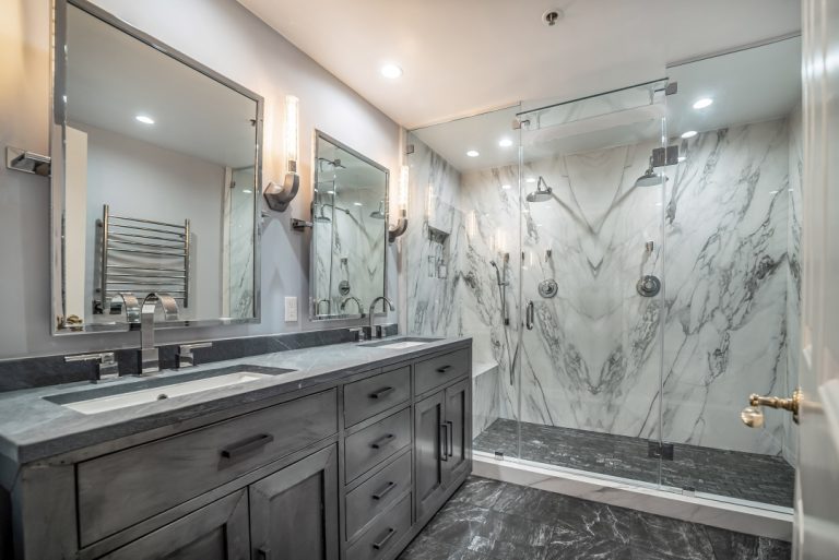 Gray double vanity beside glass shower and veined wall tile.
