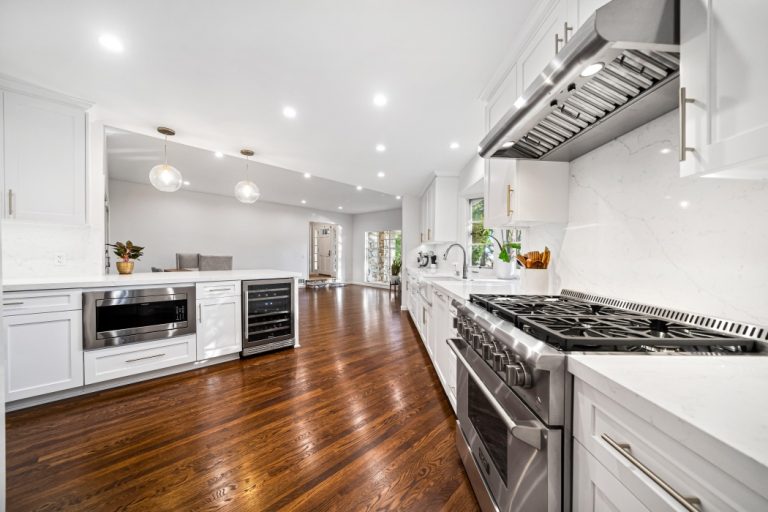 White kitchen cabinetry and gas range beside dark wood flooring.