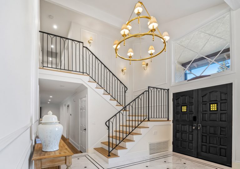 Double-height entry with circular chandelier and black stair railing.