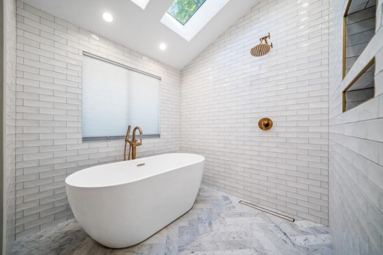 Freestanding tub beside gold-toned shower fittings and white tile.