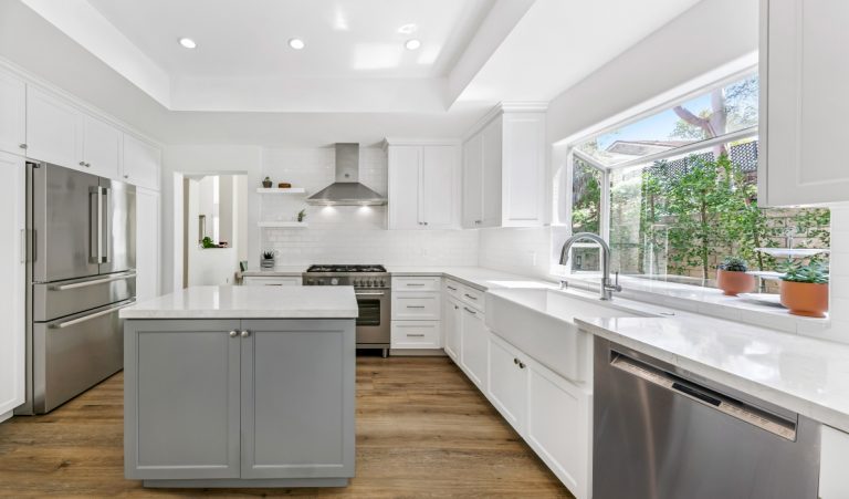 Gray kitchen island beside white cabinetry and a large sink window.