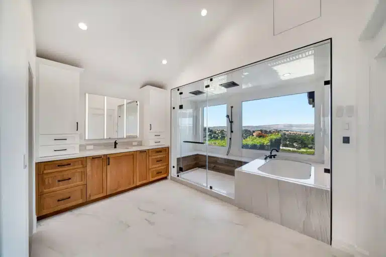Wood vanity and glass bathing area with clear windows overlooking the landscape.