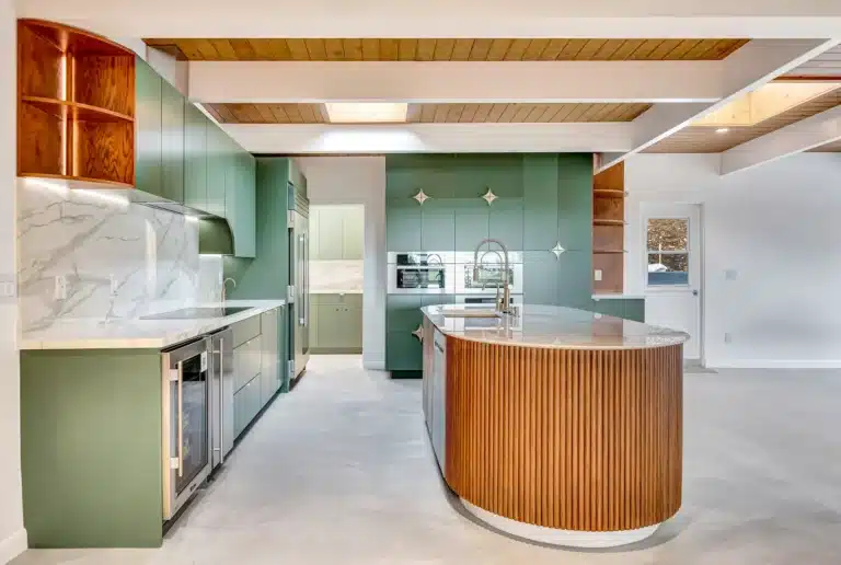 Rounded island end beside green cabinetry and veined white surfaces.