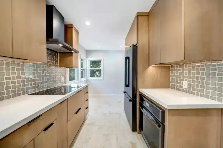 Kitchen aisle with wood cabinets and a small-format tiled backsplash.