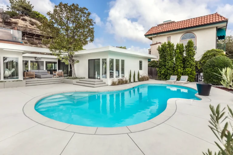 Curved swimming pool and paved patio beside the home.