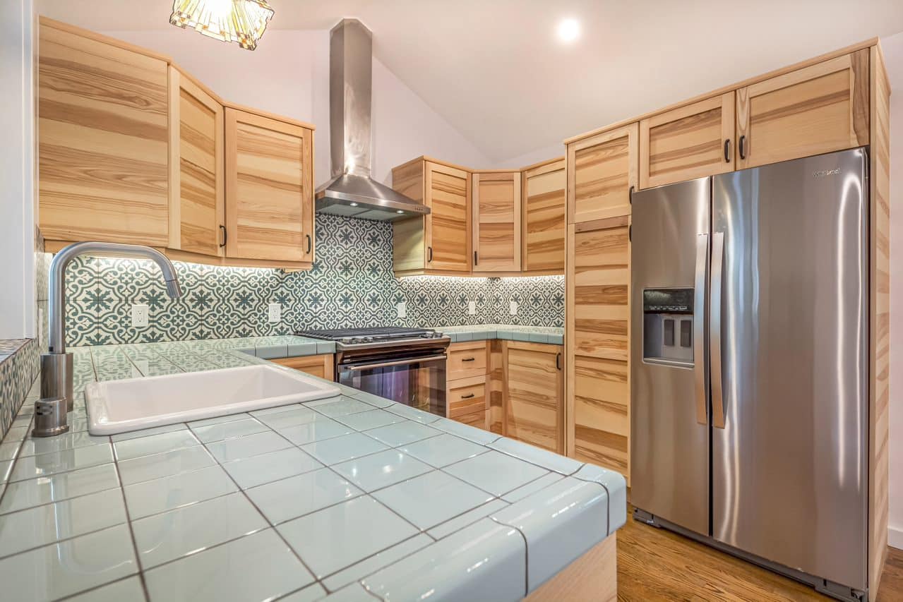 Kitchen peninsula with tiled counter beside stainless steel refrigerator.