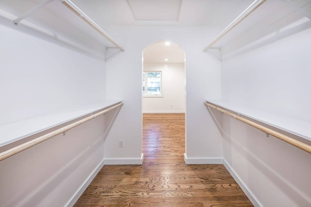 Closet with hanging rails leading through an arched doorway.