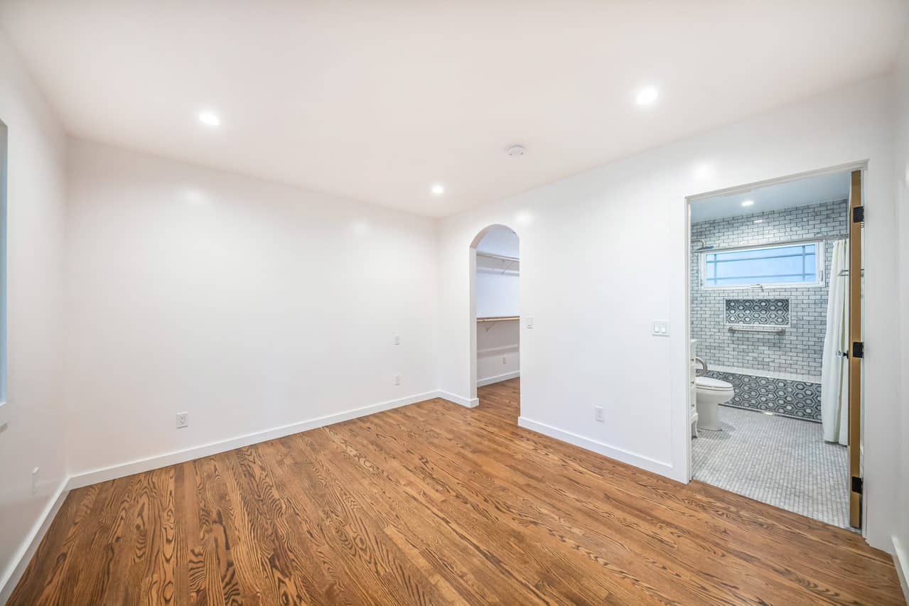 Unfurnished room with wood flooring and an adjoining tiled bathroom.