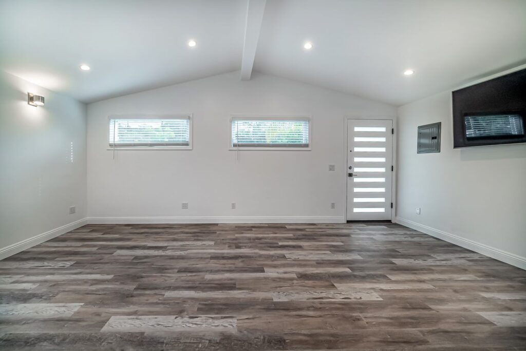 Open living area with wood-look floor and high windows.