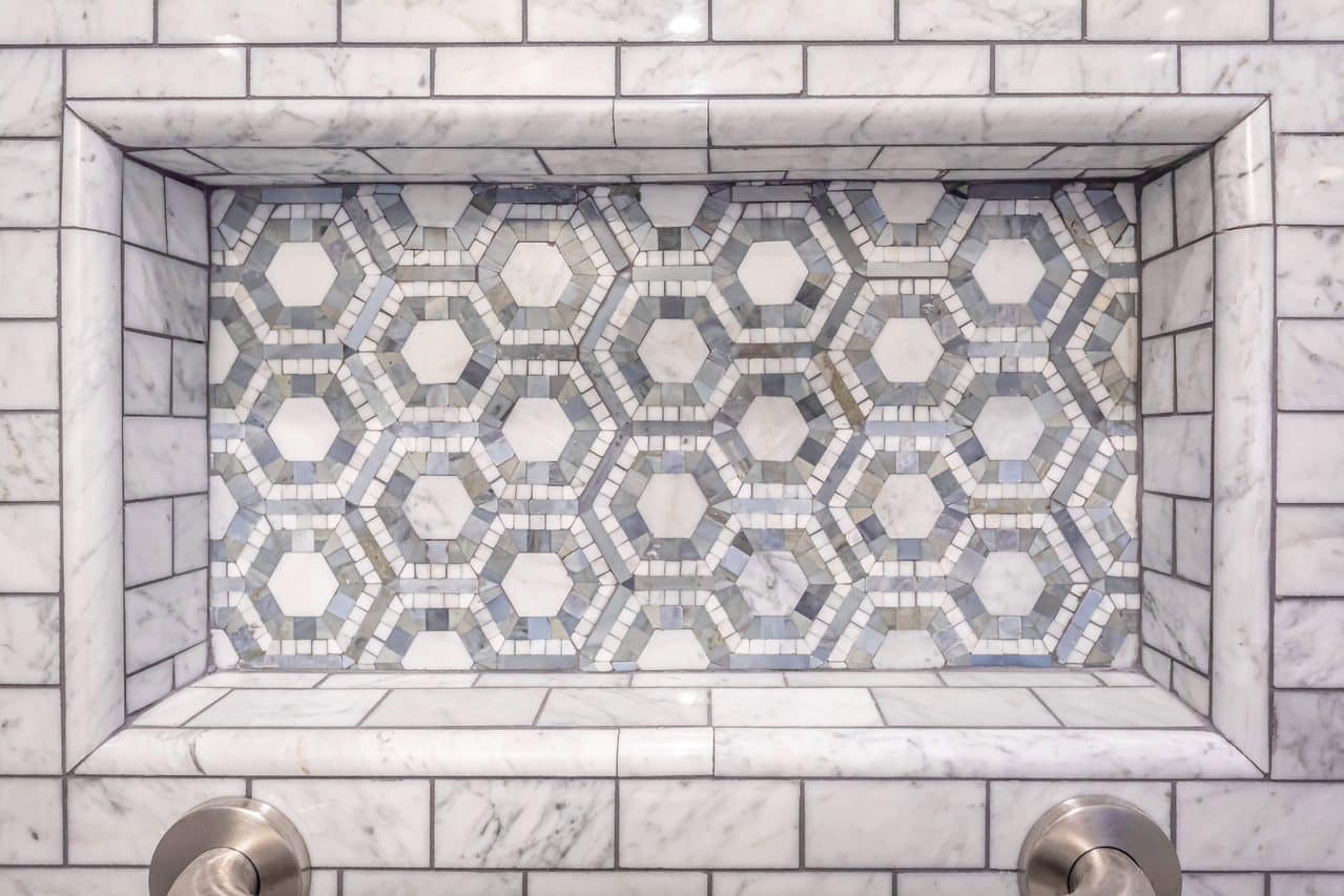 Recessed shower niche lined with patterned hexagonal tile.