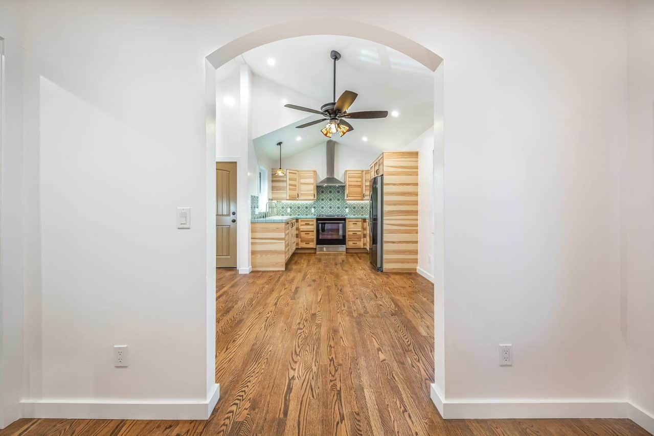 Arched opening from a white room into the wood-floored kitchen.