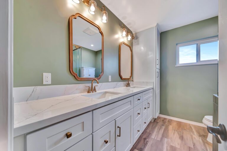 Gray double-sink vanity with drawers and cabinets beside a green wall and a small window.